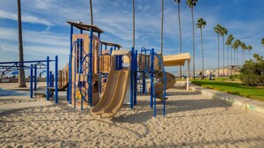 Un parque infantil con toboganes y estructuras para escalar, rodeado de palmeras y una playa de arena.