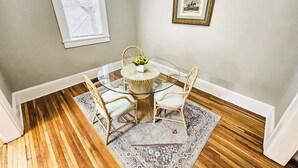 A dining area with a glass table, wicker chairs, a patterned rug, and a framed picture on the wall. - Modern Apt 86" TV! (Charlotte)