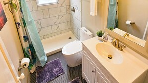 A bathroom with a bathtub, toilet, sink, and a window. - Modern Apt 86" TV! (Charlotte)