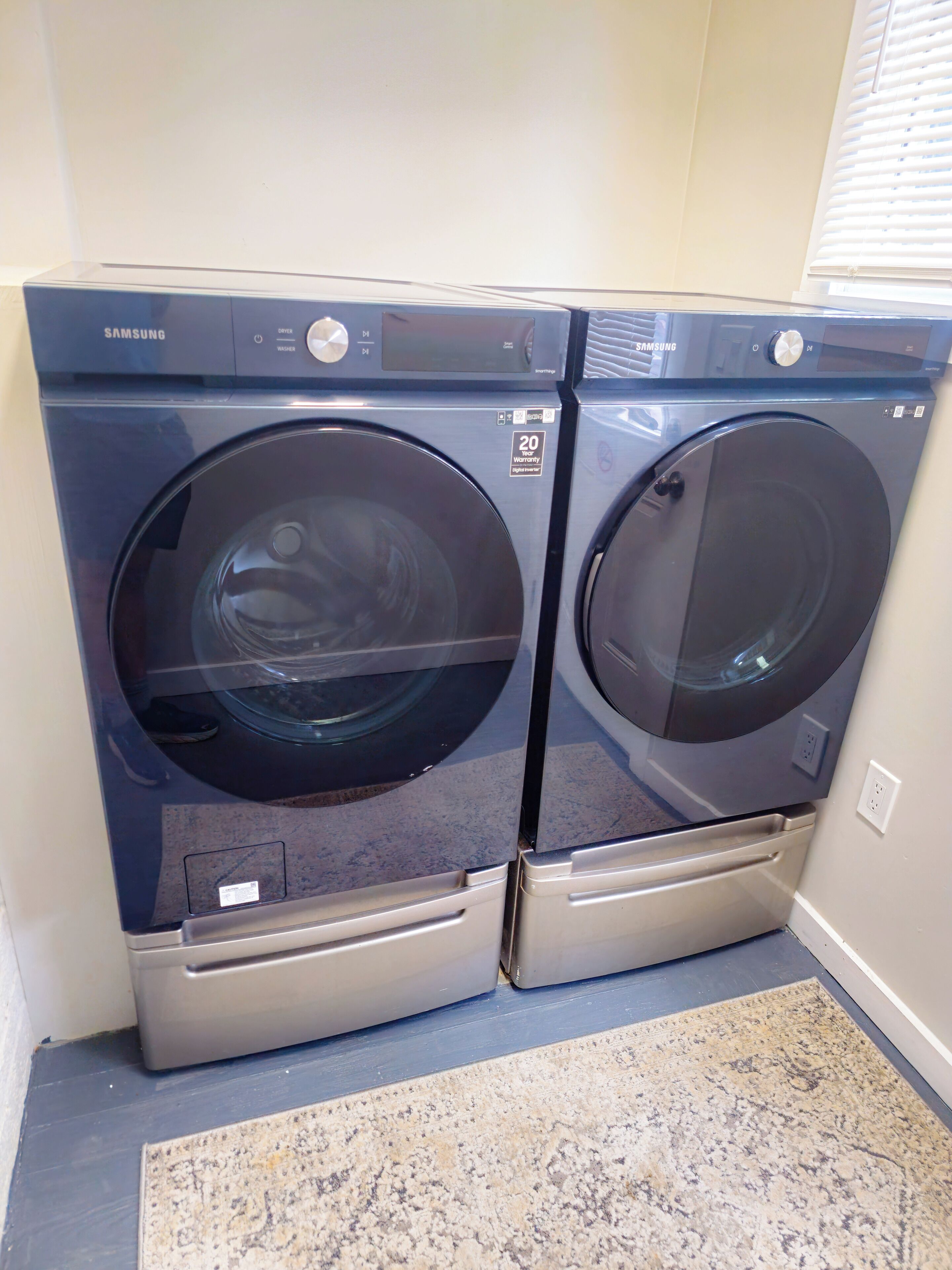 Two Samsung front-loading washing machines in a laundry room with a patterned rug on the floor.