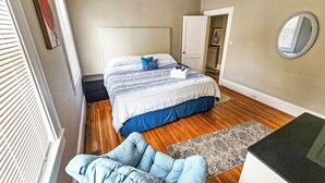 A bedroom with a bed, a ceiling fan, a mirror, and a wooden floor. - Modern Apt 86" TV! (Charlotte)