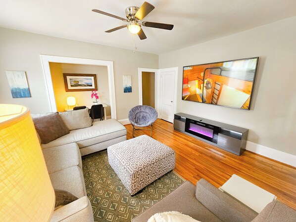 A modern living room with a sofa, ottoman, and a flat-screen TV mounted on the wall.