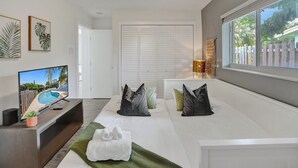Une chambre d’hôtel moderne dotée d’une grande fenêtre, d’un téléviseur à écran plat, d’un canapé avec des coussins, d’un tapis vert et d’une porte blanche.