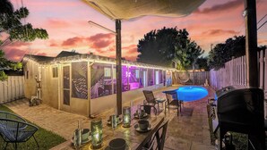 Un espace extérieur aménagé avec une terrasse, une piscine, un coin salon couvert illuminé de guirlandes lumineuses et une table à manger dressée pour un repas.