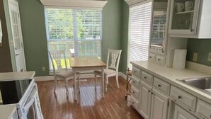 A kitchen with wooden floors, white cabinets, a dining table with chairs, and a window with blinds.