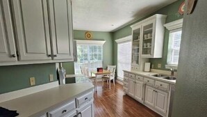 A kitchen with white cabinets, a wooden floor, and a dining area with a table and chairs.