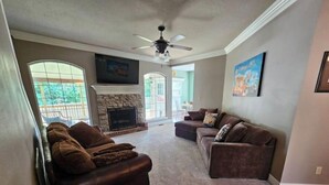 A living room with a fireplace, a ceiling fan, and a large window.