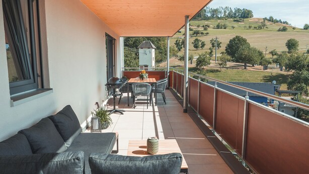 Een overdekt balkon met een bank, een tafel en uitzicht op het landschap.