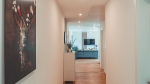 Een hal met houten vloer, een moderne keuken in de achtergrond en een groot abstract schilderij aan de linker muur.