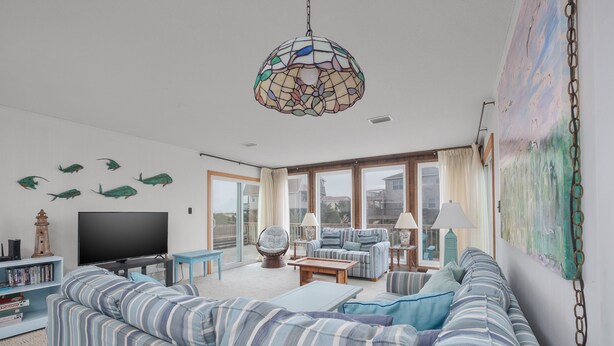 En stue med en stribet sofa, et fjernsyn, en bogreol og et stort vindue med gardiner.