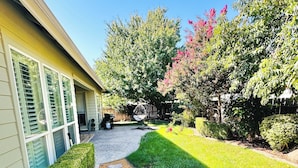 A well-maintained garden with a stone pathway leading to a house with large windows and a swing chair.