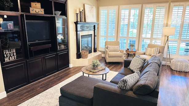 A living room with a dark wood floor, a sectional sofa, a fireplace, and large windows.