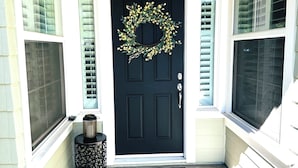 A black front door with a wreath, a small table with a lantern, and a doormat.