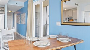 A dining area with a wooden table set for four, white chairs, and a mirror on the wall.