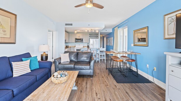 A modern living room with a blue wall, a grey leather sofa, a wooden coffee table, and a ceiling fan.