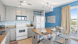 A modern kitchen with white appliances, a dining area with a table and chairs, and a view of the outdoors through a large window.