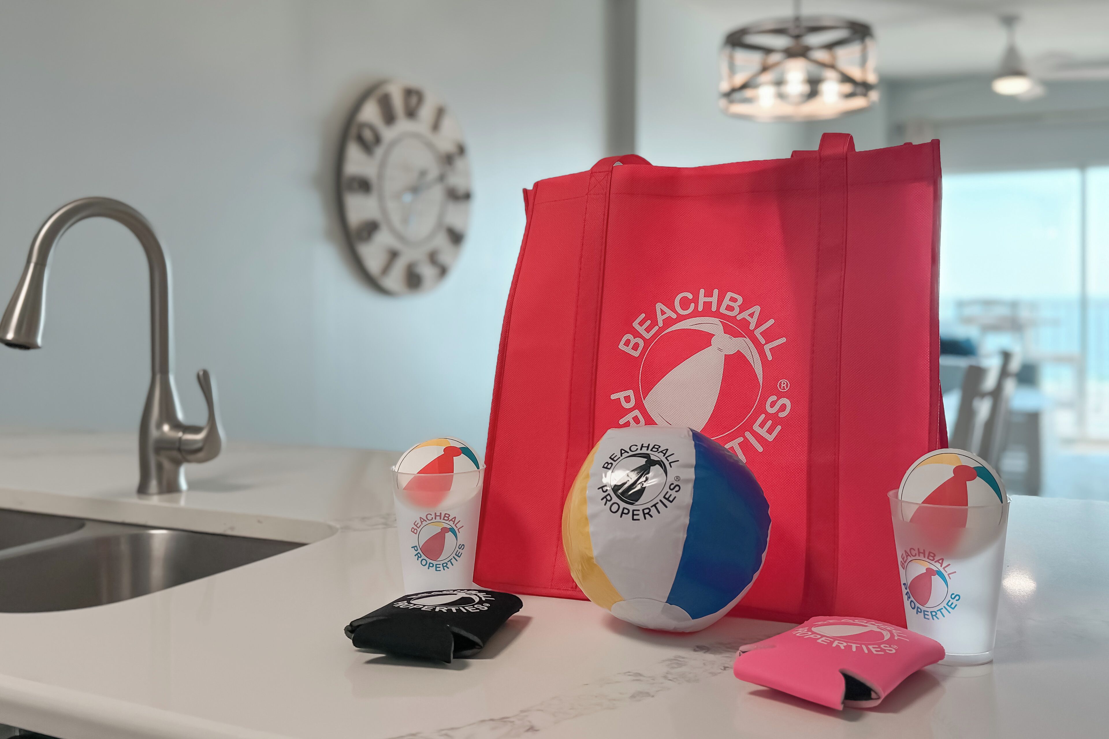 A kitchen counter with a red bag, a beach ball, and two cups with beachball properties logos.