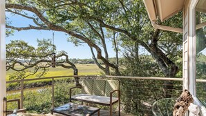 Un balcon agrémenté de meubles en osier, d’une table en verre et offrant une vue sur un paysage verdoyant.