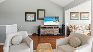 Un salon comprenant un téléviseur, deux fauteuils, un meuble en bois et des tableaux encadrés accrochés au mur.