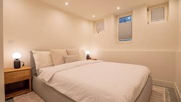 Une chambre à coucher avec un grand lit, deux tables de chevet avec des lampes, une fenêtre avec des stores et une petite étagère au-dessus de la fenêtre.