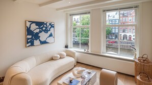 A modern living room with a curved sofa, a marble coffee table, and a view of a canal and buildings through large windows. - Elegant, sophisticated and unique canal house part of the famous canal district (Amsterdam)