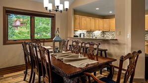 A dining room with a wooden table and chairs, a chandelier, and a view of the kitchen and outside. - A Ducking Good Time! AC, Large Deck with Hot Tub & 2 Car Garage! (Steamboat Springs)