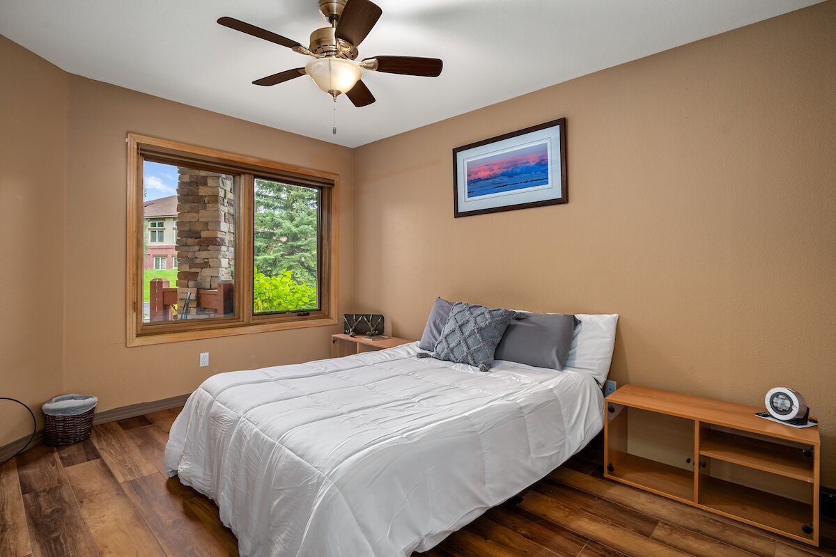 A bedroom with a bed, a ceiling fan, a window, a picture on the wall, and a wooden bench.