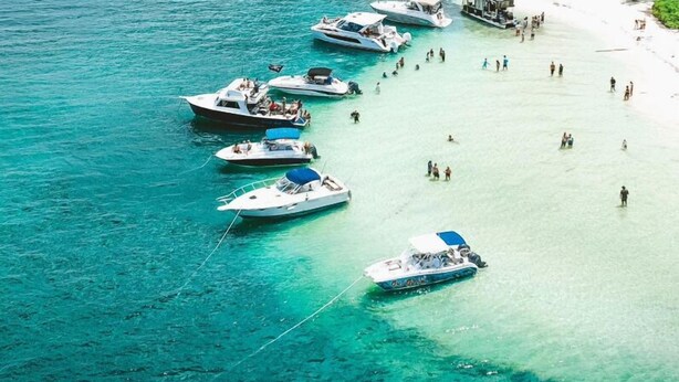Une plage où plusieurs bateaux sont amarrés près du rivage et où des personnes se promènent.