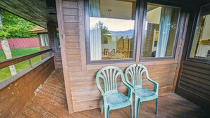 A wooden deck with two green chairs and a window overlooking a mountain landscape.