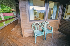 Een houten terras met twee groene stoelen en een raam met uitzicht op een berglandschap.