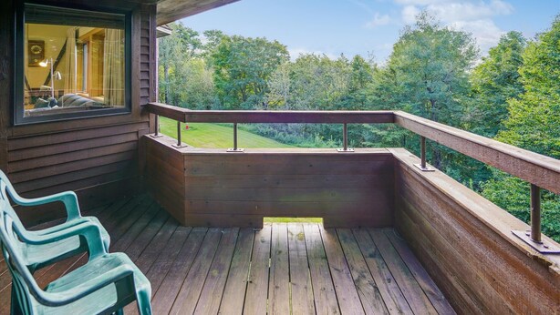 A wooden deck with a railing, a bench, and a view of a forested landscape.
