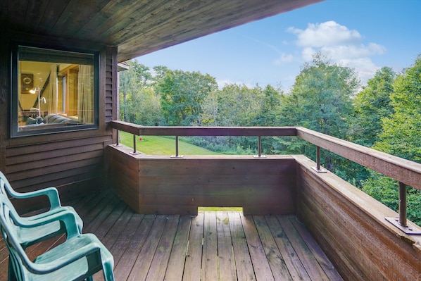 Een houten terras met een leuning, een bankje en uitzicht op een bebost landschap.