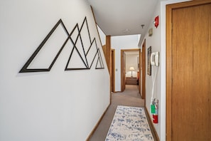 A hallway with geometric wall art, a wooden door, a telephone, and a fire extinguisher.