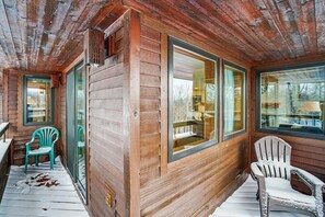 A wooden cabin with large windows, a porch with two chairs, and a visible door.