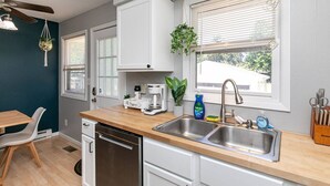 A modern kitchen with white cabinets, a wooden countertop, a built-in dishwasher, and a window with blinds. - Quaint 4bd Home - 3 min to Adventureland & Casino! (Altoona)