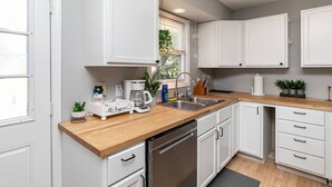 A modern kitchen with white cabinets, a wooden countertop, a dishwasher, and a coffee maker. - Quaint 4bd Home - 3 min to Adventureland & Casino! (Altoona)