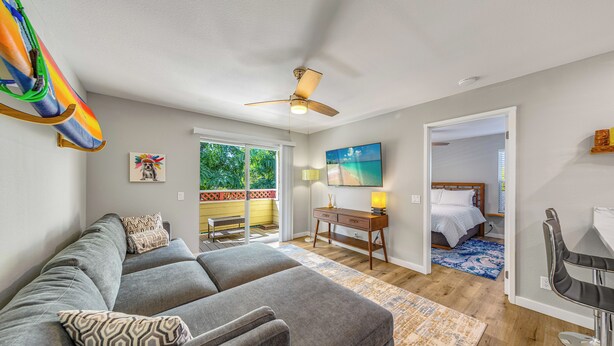 A modern living room with a grey sofa, patterned pillows, a ceiling fan, and a view of a balcony. - Updated 1 bedroom in paradise! (Waikoloa Village)