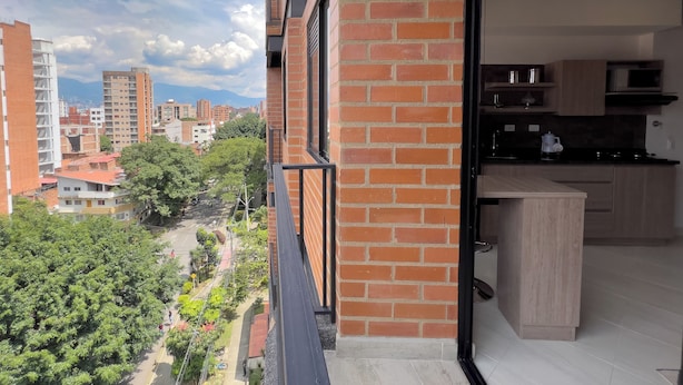 Un appartement moderne doté d’une cuisine, d’un balcon offrant une vue sur la ville et d’un mur en briques.