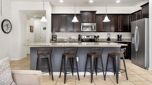 A modern kitchen with dark wood cabinets, stainless steel appliances, and a central island with bar stools. - Windsor Peace | Pool Home Near Attractions (Kissimmee)