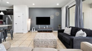 A modern living room with a sofa, ottoman, and a flat-screen TV mounted on the wall. - Windsor Peace | Pool Home Near Attractions (Kissimmee)