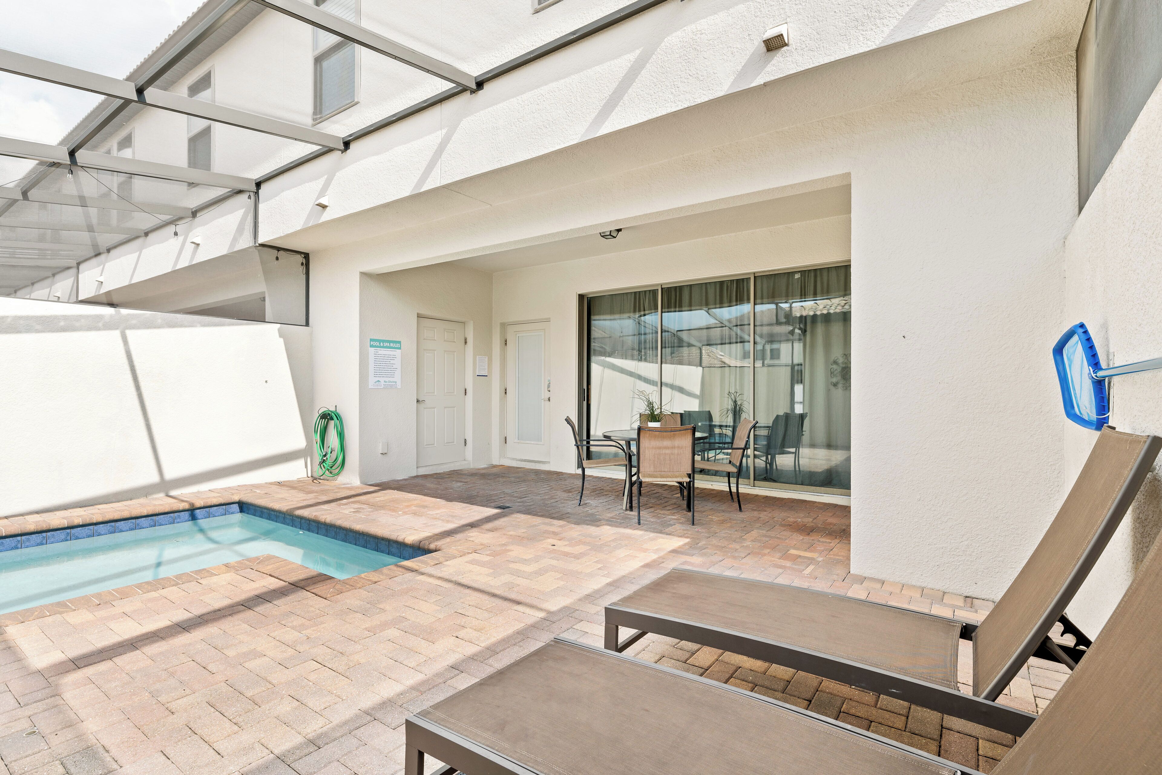 Área de piscina externa com porta de vidro que dá para um terraço coberto.