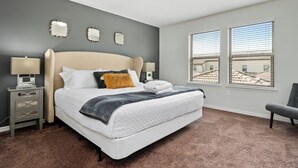 A bedroom with a large bed, two bedside tables, a chair, and a view of buildings through the windows. - Windsor Peace | Pool Home Near Attractions (Kissimmee)