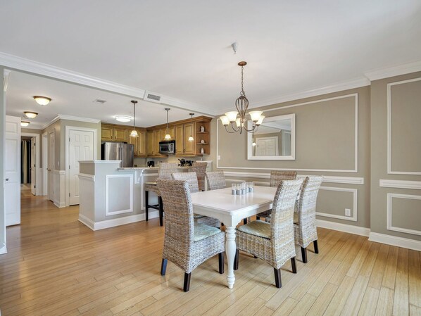 Una cocina amplia con una isla central, armarios de madera y un comedor con sillas de mimbre y una mesa blanca.