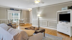 Una sala de estar con sofá, sillón, mesa de centro, mueble para televisión y lámpara de pie.