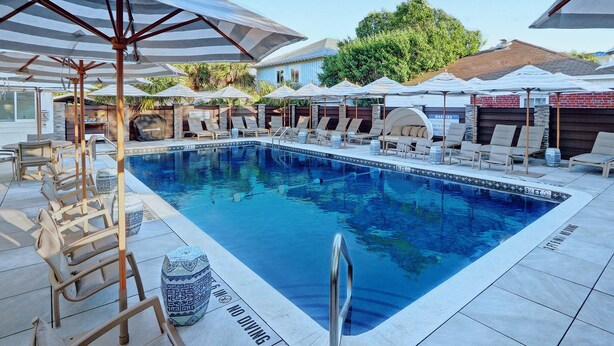 A swimming pool with lounge chairs and umbrellas, surrounded by a tiled deck and a stone wall.
