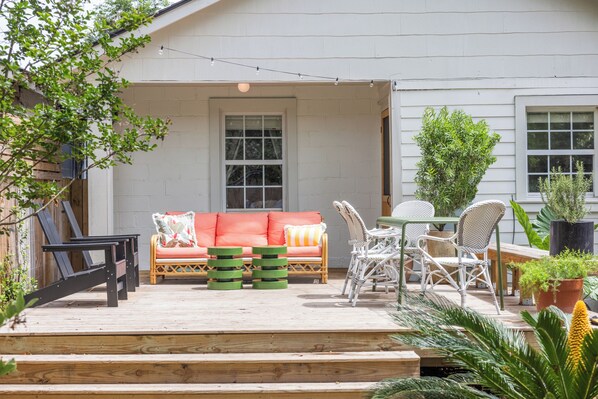 A covered patio with outdoor furniture, a wooden deck, and potted plants. - Cottage Near Forsyth Park, Heated Pool Access (Savannah)
