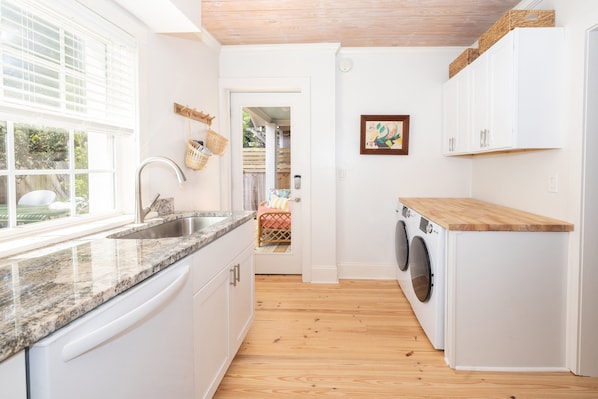 A kitchen with a granite countertop, white cabinets, a built-in washing machine, and a window with blinds. - Cottage Near Forsyth Park, Heated Pool Access (Savannah)