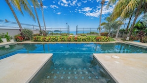A swimming pool with clear water, surrounded by palm trees and colorful flowers, with a view of the ocean in the background. - Beachfront Villa Elysian Sol Suite Sleeps 3 (Provincia de Guanacaste)