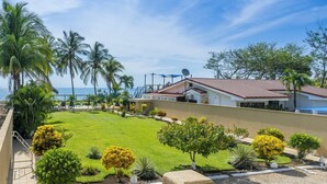 A residential property with a well-maintained lawn, palm trees, and a view of the ocean. - Beachfront Villa Elysian Sol Suite Sleeps 3 (Provincia de Guanacaste)