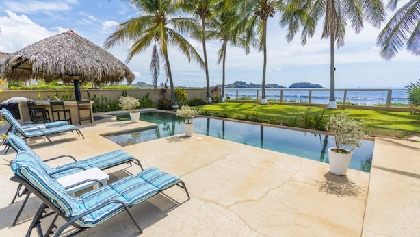A poolside area with lounge chairs, a thatched umbrella, and a view of the ocean. - Beachfront Villa Elysian Sol Suite Sleeps 3 (Provincia de Guanacaste)